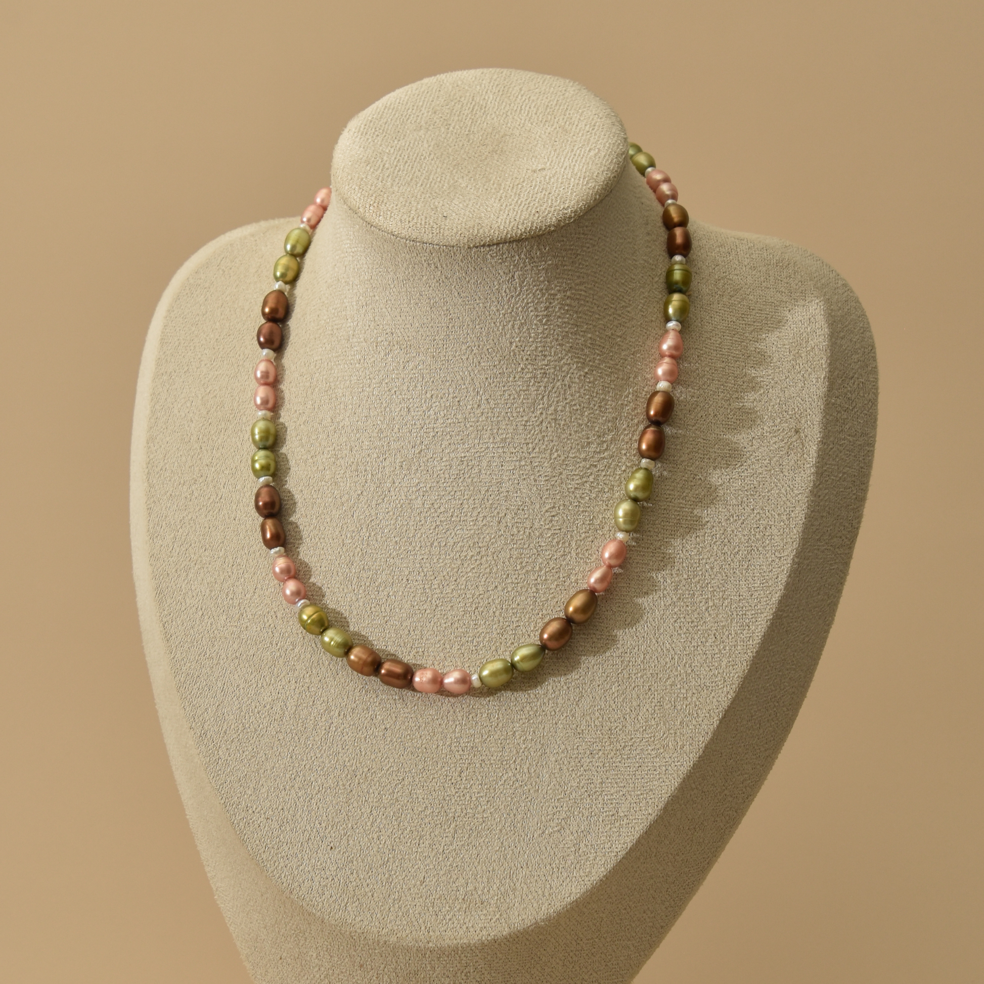 A multi-colored freshwater pearl necklace displayed on a textured beige jewelry bust against a solid warm beige background.