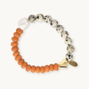 A beaded stretch bracelet featuring orange beads, speckled cream and black Dalmatian-style beads, a white stone bead, and two gold heart charms, one of which is engraved with the name 'Diane'.