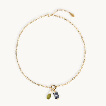 A gold chain necklace with a small ring charm holding an olive green bead and a navy blue patterned pouch, displayed on a clean off-white background.