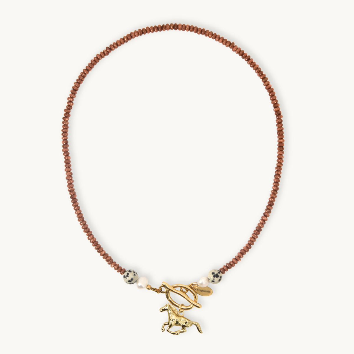 A delicate necklace featuring a strand of small glittery orange beads, accented with white beads, a gold toggle clasp, and a gold horse charm, displayed on a clean off-white background.