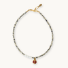 A delicate beaded necklace with black and white beads, a small cluster of white pearls, and a gold-tone charm featuring a red enamel heart with a gold 'F' monogram, displayed on a light cream background.