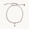 A delicate adjustable cord necklace featuring a small white shell pendant and a tiny gold tag, displayed on a clean off-white background.