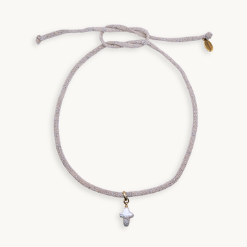 A delicate adjustable cord necklace featuring a small white shell pendant and a tiny gold tag, displayed on a clean off-white background.