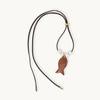 A fish-shaped pendant necklace with a textured reddish-brown glitter finish, suspended from a dark brown cord with small white beads and gold-toned hardware, shown on a light cream background.