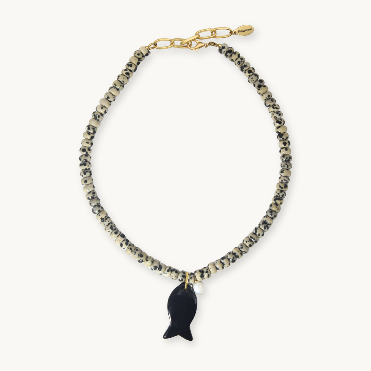A beaded necklace featuring textured black and beige beads, a gold-tone chain clasp, and a glossy black fish-shaped pendant, displayed on a clean off-white background.