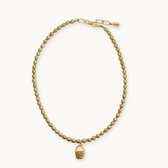 A gold beaded necklace with a small woven basket charm, displayed on a clean off-white background.