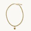 A gold beaded necklace with a small woven basket charm, displayed on a clean off-white background.