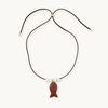 A black cord necklace with a small brown textured fish pendant, accented by three white beads and gold-tone hardware, displayed on a light cream background.