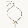 A black cord necklace with a fish-shaped pendant, a small tiger's eye bead, and a brown rectangular charm, displayed on a light cream background.
