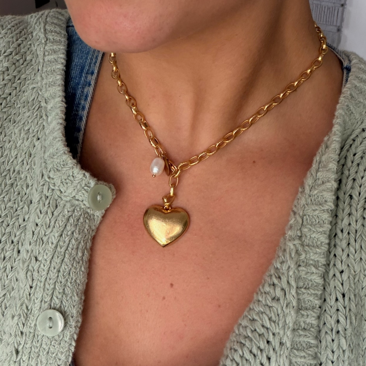 Gold chain necklace with a puffed heart pendant worn over an open denim shirt