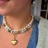Layered freshwater pearl necklace and gold chain with a heart pendant worn over denim