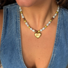 Pearl and stone beaded necklace with a gold heart pendant worn over an open denim shirt
