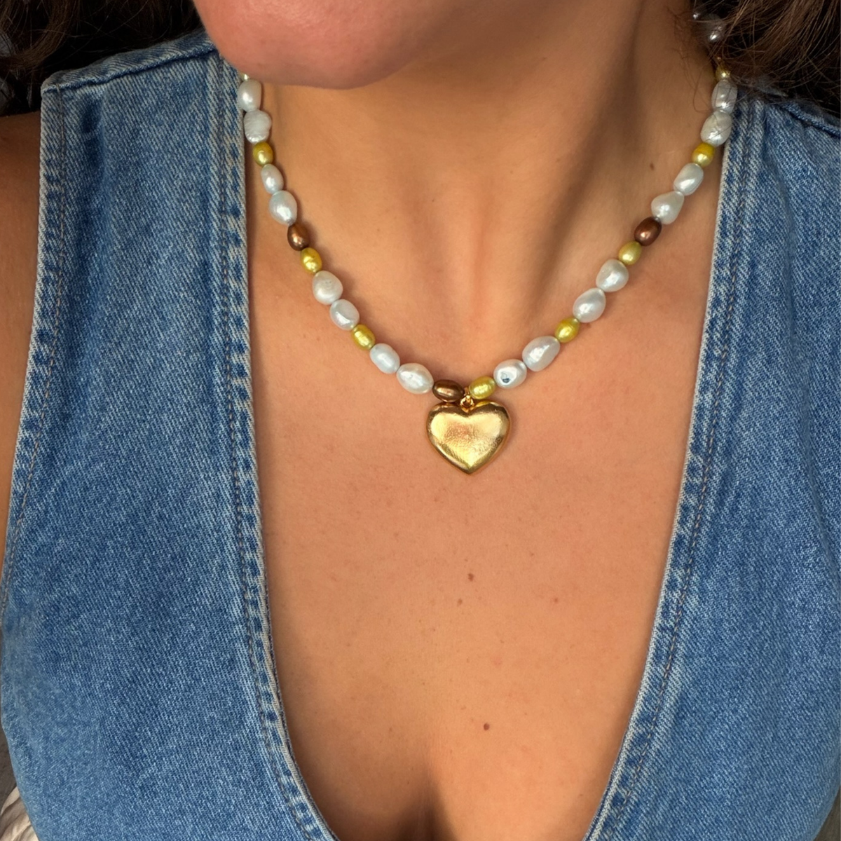 Pearl and stone beaded necklace with a gold heart pendant worn over an open denim shirt
