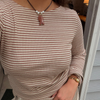 A close-up of a person wearing a beige and brown horizontally striped long-sleeve top, accessorized with a necklace and a gold watch.