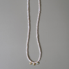 A long strand of white freshwater pearls draped vertically on a neutral gray background, featuring three small gold-toned decorative charms at the bottom.