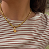 A close-up of a person wearing a golden green pearl necklace with a small basket shaped pendant, paired with a brown and cream striped top.