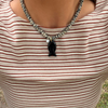 A close-up of a person wearing a beaded necklace with a black pendant over a beige and brown horizontally striped shirt.