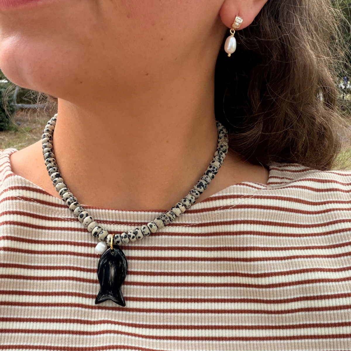 A close-up lifestyle shot of a woman wearing a handmade beaded necklace with a black fish pendant and a matching beaded earring.