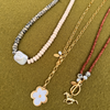 Three handcrafted necklaces on an olive green knit. A strand of dalmatian-spotted and cream rondelles centers on a large baroque pearl, beside a golden chain with a white flower pendant and a rust-red strand finished with a golden horse charm.