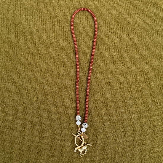 Rust-red sparkly rondelle necklace with dalmatian stones and pearls at each end, joined by a golden toggle clasp with a galloping horse charm.