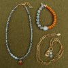 Flat lay of the dalmatian ladybug necklace with its pearl section, the dalmatian and orange heart bracelet, and a coiled golden paperclip chain with a cowboy hat charm.