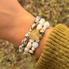 Wrist stacked with the dalmatian and pearl heart bracelet and a second bracelet of baroque pearls with pale blue and green stones, against grass.