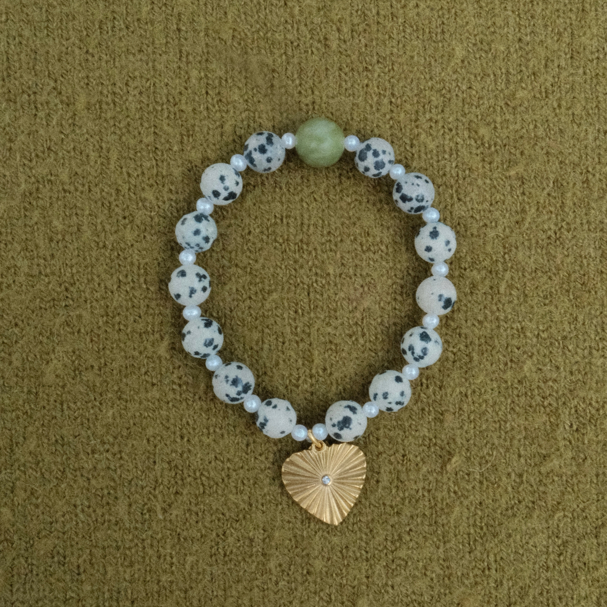 Stretch bracelet of dalmatian-spotted stones and tiny freshwater pearls with one green stone, finished with a ribbed golden heart charm set with a small crystal.