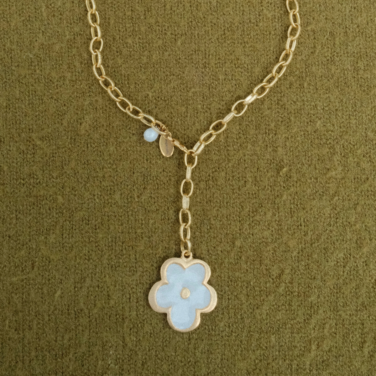 Golden chain lariat necklace ending in a pearl flower pendant, with a pearl drop and Fraypearls tag at the clasp, on olive green knit.