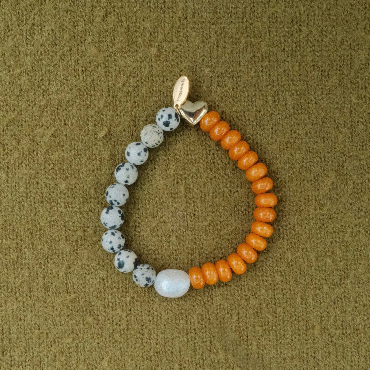 Bracelet half dalmatian-spotted stones and half bright orange rondelles, joined by a freshwater pearl and a golden puffed heart with a Fraypearls tag.