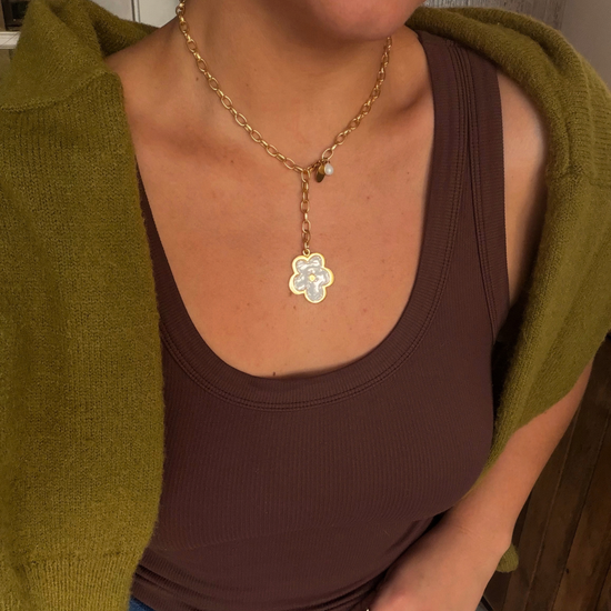 Woman in a brown ribbed tank and olive cardigan wearing a golden chain lariat with a white flower pendant and a pearl drop.