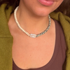 Close-up of a strand of cream rondelles and dalmatian-spotted stones meeting at a rectangular baroque pearl, worn with a brown tank and olive cardigan.