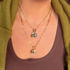Two layered golden paperclip chains. The shorter holds a pearl, green stone and blue and white ceramic charm, and the longer holds a golden cowboy hat charm, a pearl and a dalmatian stone.