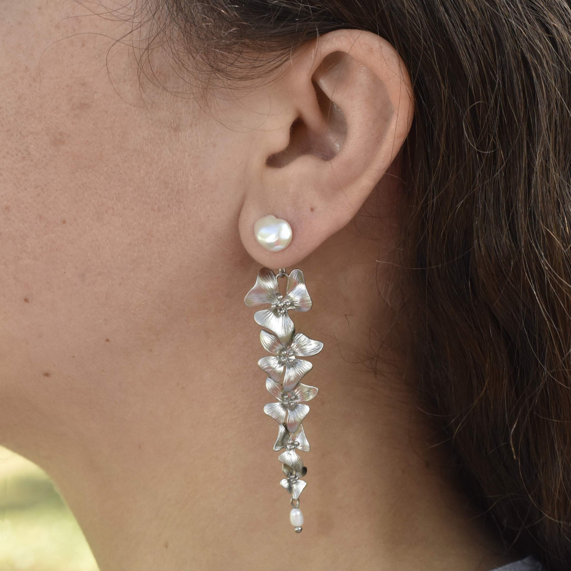 Close-up of a woman's ear wearing a dangling earring with cascading metallic flowers and a pearl stud, conveying elegance and sophistication.