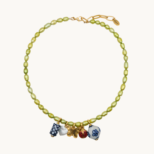 A necklace with green pearls and colorful charms, including a gold butterfly, ladybug, and floral beads. The tone is playful and elegant.