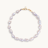 A baroque pearl necklace with irregular white pearls strung along a delicate lilac string. The lustrous pearls convey an elegant, natural look.