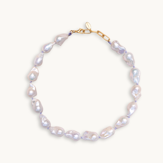 A baroque pearl necklace with irregular white pearls strung along a delicate lilac string. The lustrous pearls convey an elegant, natural look.