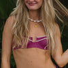 Close-up of a woman adorned with a chunky pearl necklace and a gold pendant necklace. She wears a magenta top with white trim.