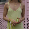 A person in a light green dress holds a sliced kiwi in one hand, with the other hand adorned with lime green beads, pearls, and gold bracelets.