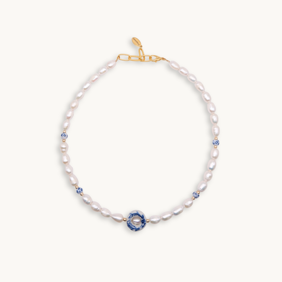 Elegant necklace featuring white pearls with blue floral ceramic bead accents and a gold clasp. The design conveys a sense of classic sophistication.
