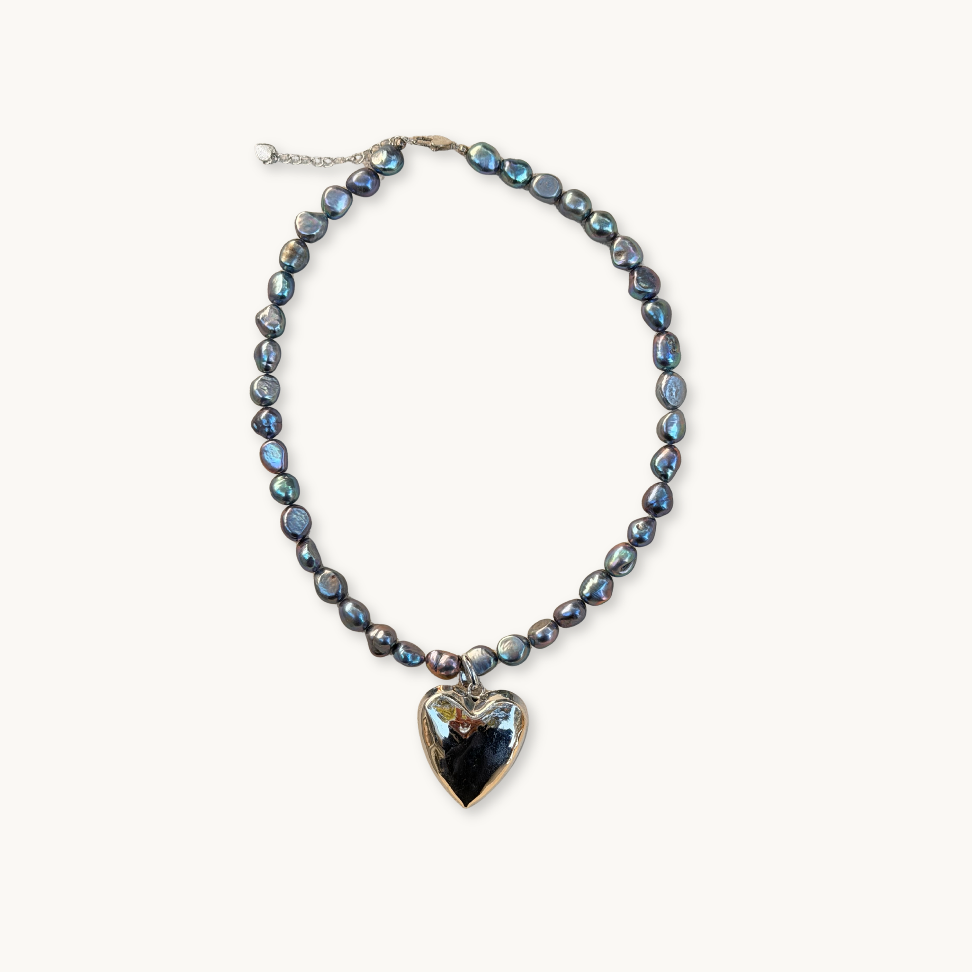 String of dark iridescent pearls with a reflective silver heart pendant, set on a neutral background. Elegant and sophisticated design.