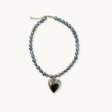 String of dark iridescent pearls with a reflective silver heart pendant, set on a neutral background. Elegant and sophisticated design.
