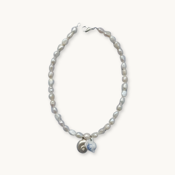 A necklace with irregular pearls features a metal clasp. The centerpiece includes a small spiral shell and a white pendant with blue detailing, exuding an elegant, coastal vibe.