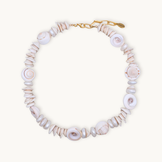 A necklace made of spiral-shaped white shells linked by small beads, featuring a gold clasp. The design exudes a natural, beachy elegance.