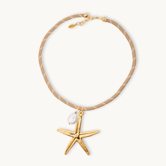 Beige rope choker necklace with a gold starfish charm and a white pearl accent. Features delicate textures, exudes a coastal, elegant vibe.