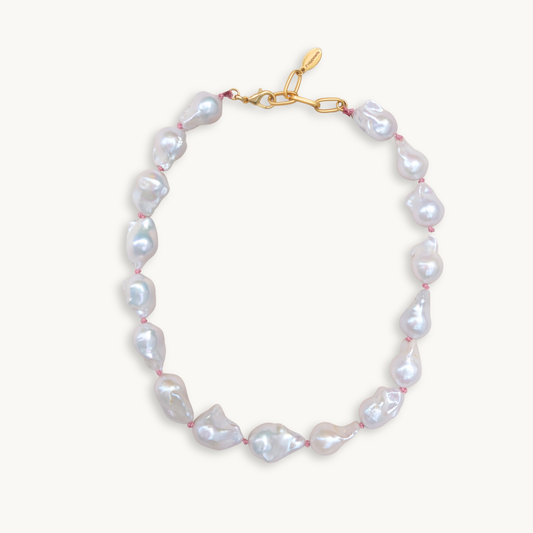 A baroque pearl necklace with irregular white pearls strung along a delicate pink string. The lustrous pearls convey an elegant, natural look.