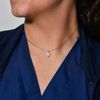 Close-up of a person wearing a delicate gold chain necklace with a small pearl pendant, set against a dark blue collared shirt. The mood is elegant.