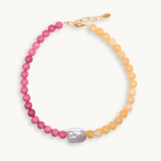Necklace with alternating pink and yellow beads, featuring a large central irregular pearl and a gold clasp. The design feels vibrant and elegant.