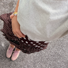 A person is standing on a pavement wearing a gray top, a brown polka-dot skirt, a pink stone and pearl bracelet, and pink sneakers. Their hand rests on their hip.