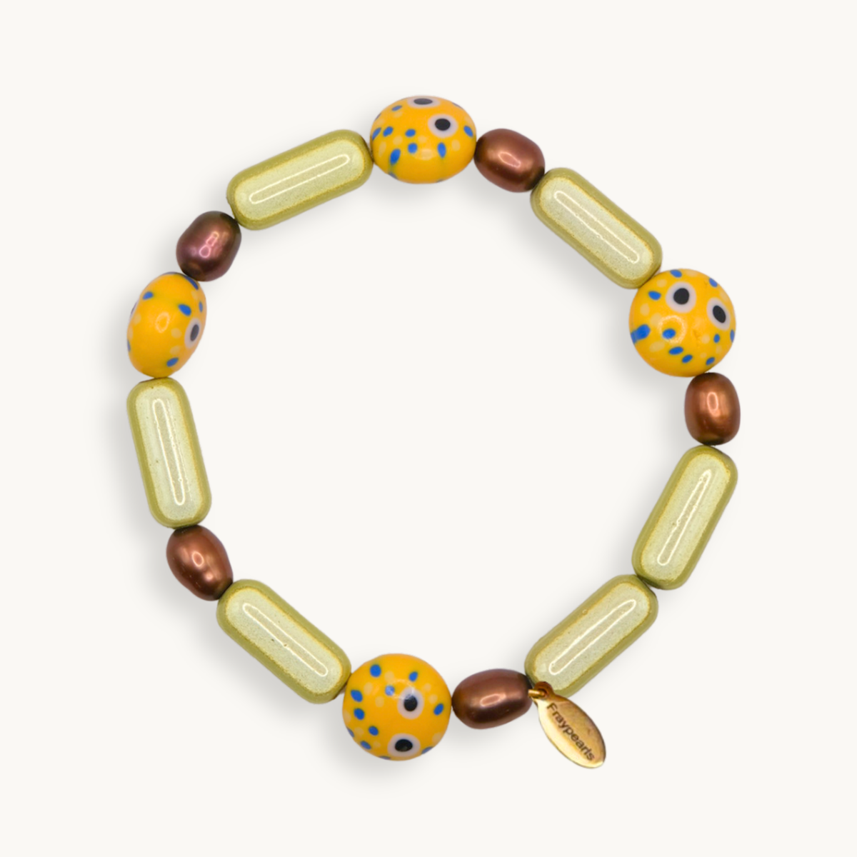 A handmade beaded bracelet with olive-green capsule beads, yellow-orange round beads with blue and black speckles, and metallic bronze oval beads, displayed on a light cream background.
