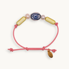 A pink cord bracelet with a sliding knot closure, decorated with a blue and white agate bead, two pink freshwater pearls, and two gold capsule beads. A small gold tag attached to the cord.